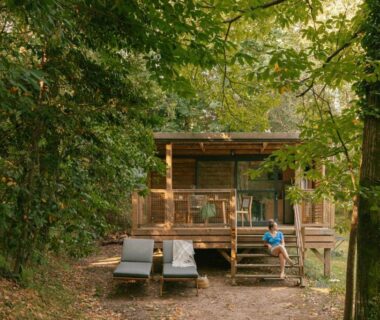 Terrasse en bois avec transats et personne assise dans la forêt au Slow Village Anduze Cévennes