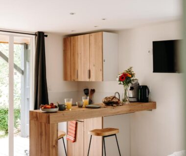 Intérieur coin cuisine avec bar tabourets et baie vitrée dans le locatif Slow Village Séveilles