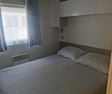 Chambre avec lit double oreillers fenêtre et rangements au camping Soleil Luna
