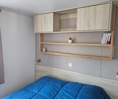 Chambre avec lit couvert d'une couette bleue et rangements dans le mobil home Sous les Pins
