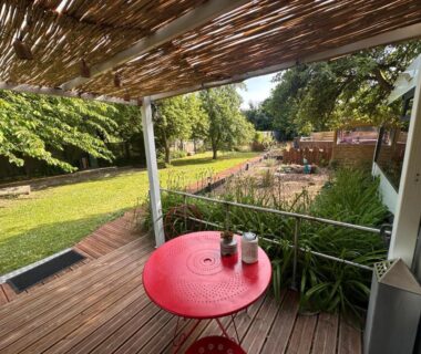 Terrasse ombragée avec table rouge et tasses et vue sur pelouse du camping TERMINUSBUS