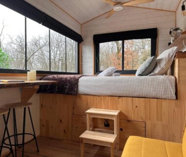 Intérieur avec lit surélevé et grandes fenêtres donnant sur la forêt dans la Tiny house romantique avec bain nordique