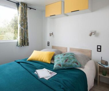 Chambre avec lit double couette turquoise et placards jaunes au camping U FARNIENTE