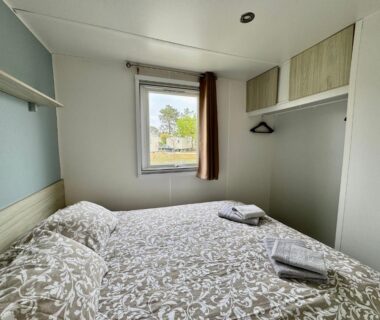Chambre avec lit double et fenêtre dans le bungalow Un toit sur le bassin camping les viviers