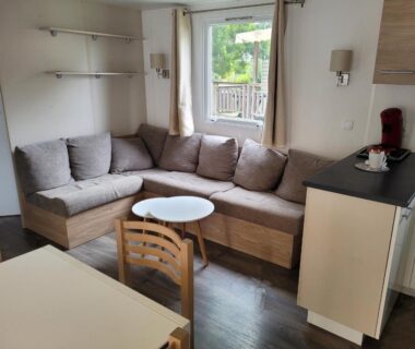 Salon avec canapé d'angle et coin repas donnant sur l'extérieur du VM-Mobile Home 3 ch