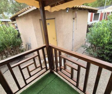 Terrasse couverte avec sol en gazon synthétique et garde-corps en bois du mobil home La Carabasse