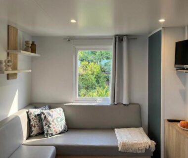Intérieur salon de mobil-home avec canapé et fenêtre donnant sur la végétation au Vista Mare