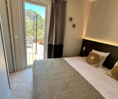 Chambre avec lit double et balcon donnant sur la végétation au camping Voltaire
