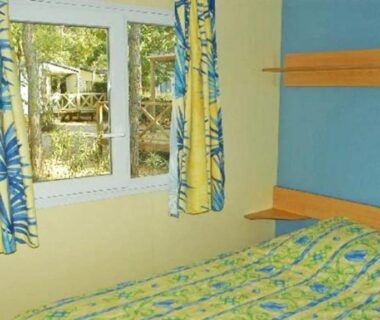 Chambre avec lit et rideaux donnant sur arbres au ZEcamping 3 étoiles chiens acceptés piscine bar et restaurant