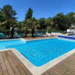 Piscine extérieure sur terrasse en bois avec palmiers et transats au ZEcamping 3 étoiles – piscine chauffée et club enfant