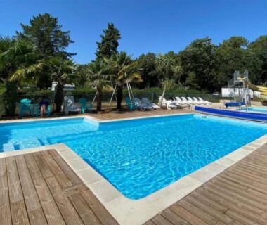 Piscine extérieure sur terrasse en bois avec palmiers et transats au ZEcamping 3 étoiles – piscine chauffée et club enfant