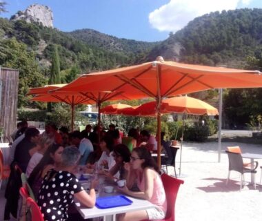 Terrasse extérieure avec parasols orange convives et montagne au ZEcamping 3 familial animaux acceptés bar piscine et soirées animées