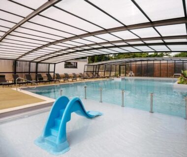 Piscine couverte avec toboggan et chaises longues dans le ZEcamping 4 étoiles animé