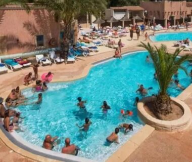Piscine extérieure animée avec baigneurs transats et palmiers au ZEcamping 4 étoiles parc aquatique hammam et restaurant