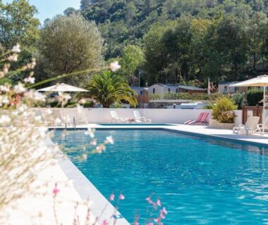 Piscine extérieure bordée de transats et parasols au ZEcamping 4 étoiles verdoyant