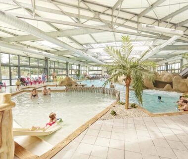 Piscine couverte avec toboggan et palmiers dans le ZEcamping 5 étoiles