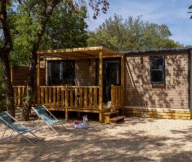 Mobil-home avec terrasse en bois et chaises longues sous arbres au ZEcamping 5 étoiles