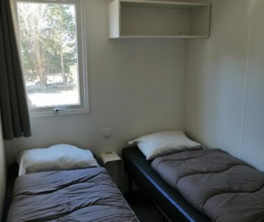 Intérieur avec deux lits simples et une fenêtre du bungalow au soleil camping les dunes