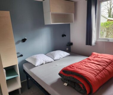Chambre avec lit double, fenêtre et couette rouge au camping les pêcheurs