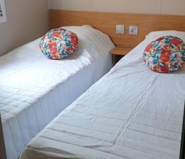 Chambre avec deux lits simples et coussins colorés dans l'hébergement du camping les sables du midi