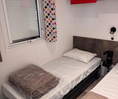 Chambre avec deux lits simples et rideau coloré dans le camping sol a gogo 3 chambres