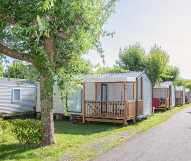 Allée de mobil-homes et petites terrasses sous arbres au camping la ferme des 4 chenes