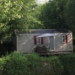 Terrasse avec table devant mobil-home entouré d'arbres à la ferme des 4 chenes