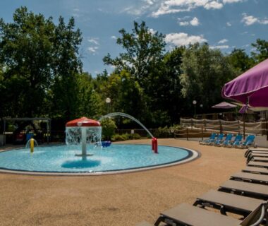 Bassin ludique pour enfants avec fontaine et transats au Camping Des 3 Lacs