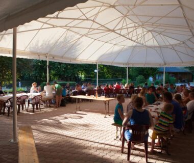 Terrasse couverte avec tables et convives au Camping Des 3 Lacs