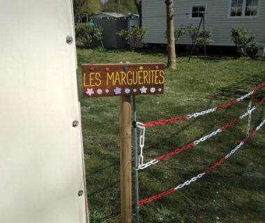 Allée herbeuse avec panneau en bois au camping Les Marguerites