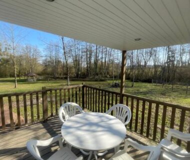 Terrasse couverte avec table et chaises donnant sur prairie et arbres du logement au coeur de la nature