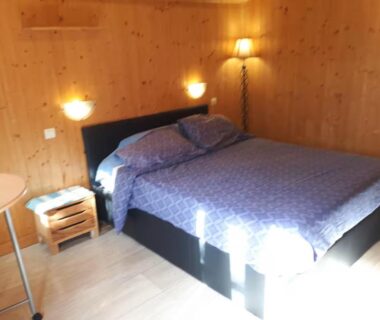 Chambre du chalet avec lit double table de chevet et lampe dans le loue chalet calme tout équipé