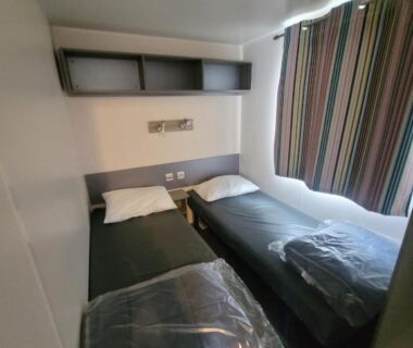 Intérieur chambre avec deux lits simples et rideau rayé dans le mobil home