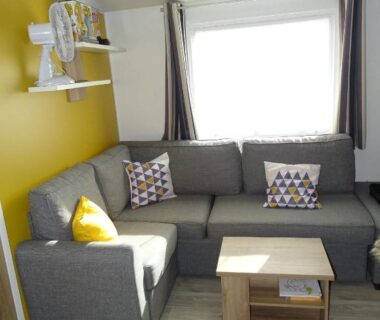 Salon avec canapé d'angle gris et mur jaune du mobil home 8 pers à Saint Jean de Monts