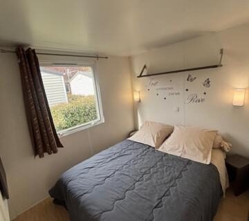 Chambre avec lit double et fenêtre dans le mobil home AU SOLEIL