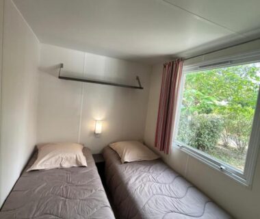 Chambre avec deux lits simples et fenêtre donnant sur la végétation du mobil home AU SOLEIL