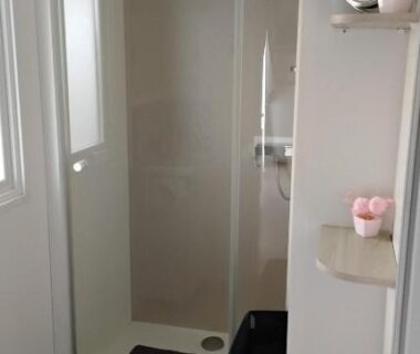 Salle de bain avec douche vitrée et panier à linge dans le mobil home le castellas Bertrand