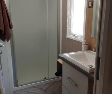 Salle de bain avec douche vitrée et lavabo dans le mobil home l'écrin bleu bougainvilliers
