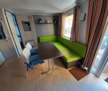 Intérieur du salon avec banquette verte et table dans le mobile home entierement équipé