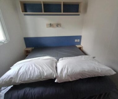 Chambre avec lit double étagères et petite fenêtre dans le mobilhome 232 Tohapi Marvilla