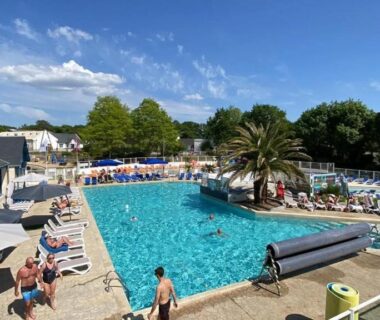Piscine extérieure avec transats et palmiers au mobilhome Pont Aven 3chbres 152 avec grande terrasse fermée