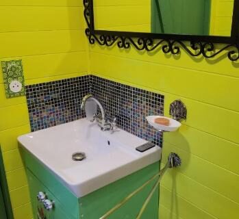 Salle de bain avec lavabo vert et miroir noir dans la roulotte Tipergwendiou