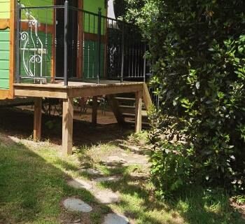 Allée de dalles menant à la terrasse en bois au milieu des arbres de la roulotte Tipergwendiou