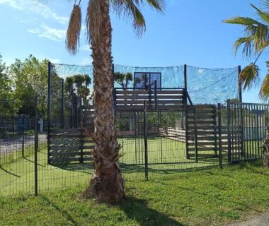Aire de jeux extérieure avec structure surélevée et palmiers au camping Sable du Midi 1